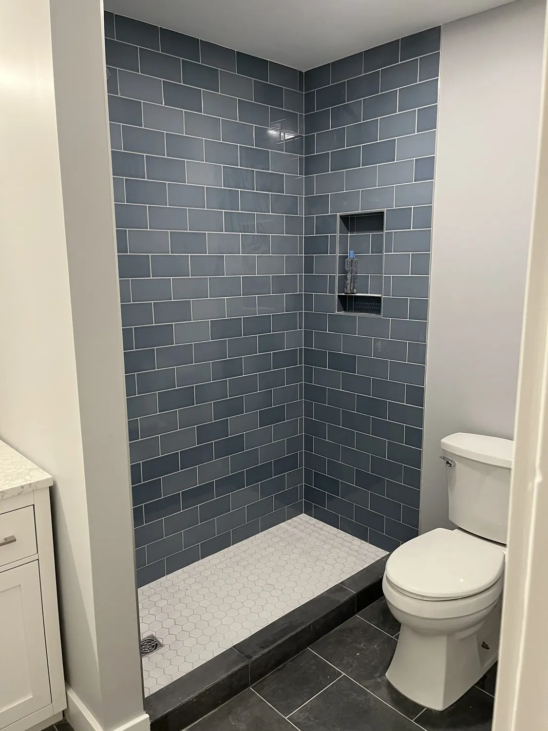 Custom walk-in shower with blue-gray subway tile and hexagon floor